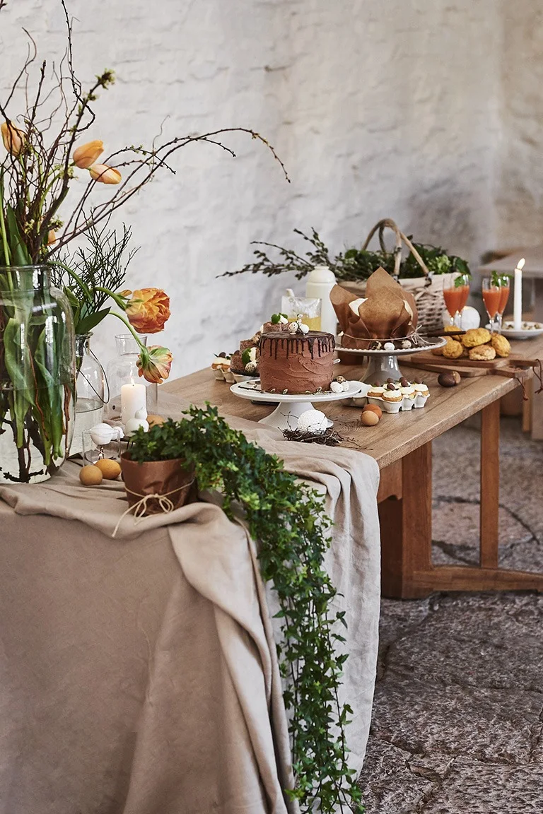Ett långbord i trä står uppdukat i rustik stil med flertalet påskdesserter på bordet som tårtor och muffins.