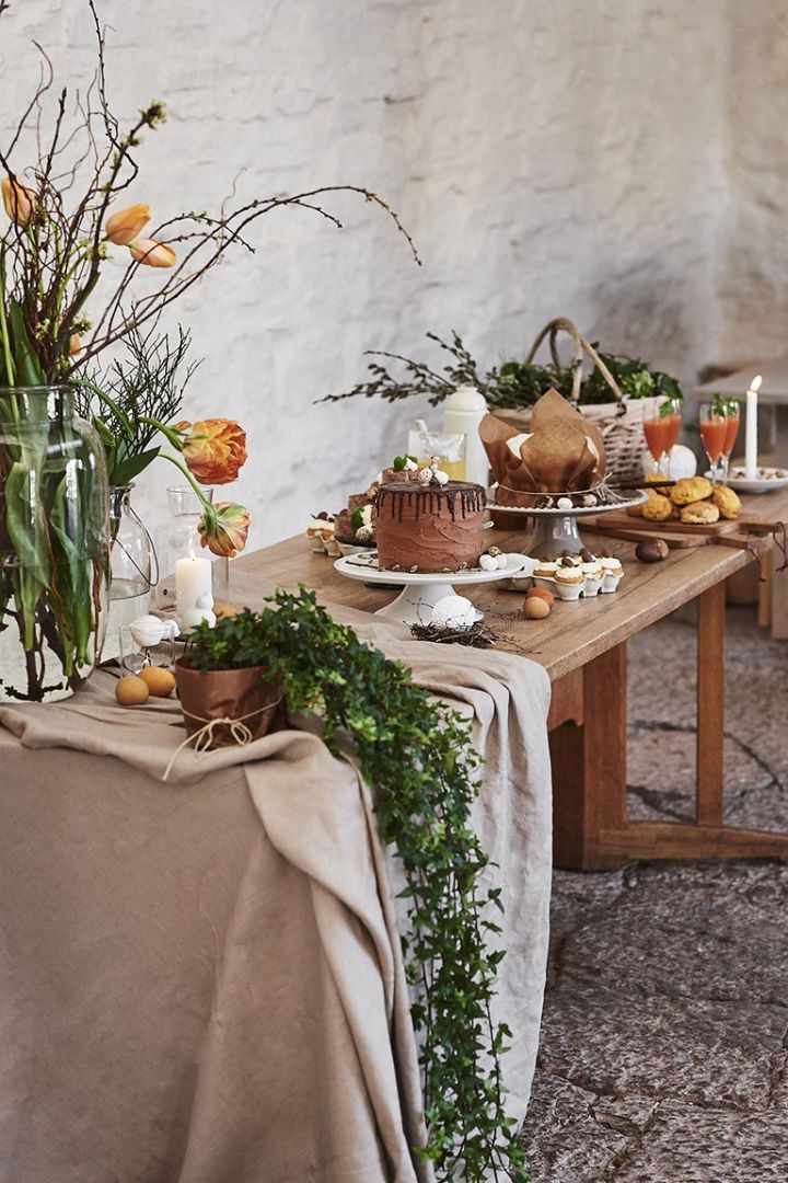 Ett långbord i trä står uppdukat i rustik stil med flertalet påskdesserter på bordet som tårtor och muffins. 