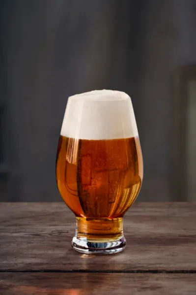 Tulpformat glas med bärnstensfärgad öl och tjockt vitt skum på ett rustikt träbord.