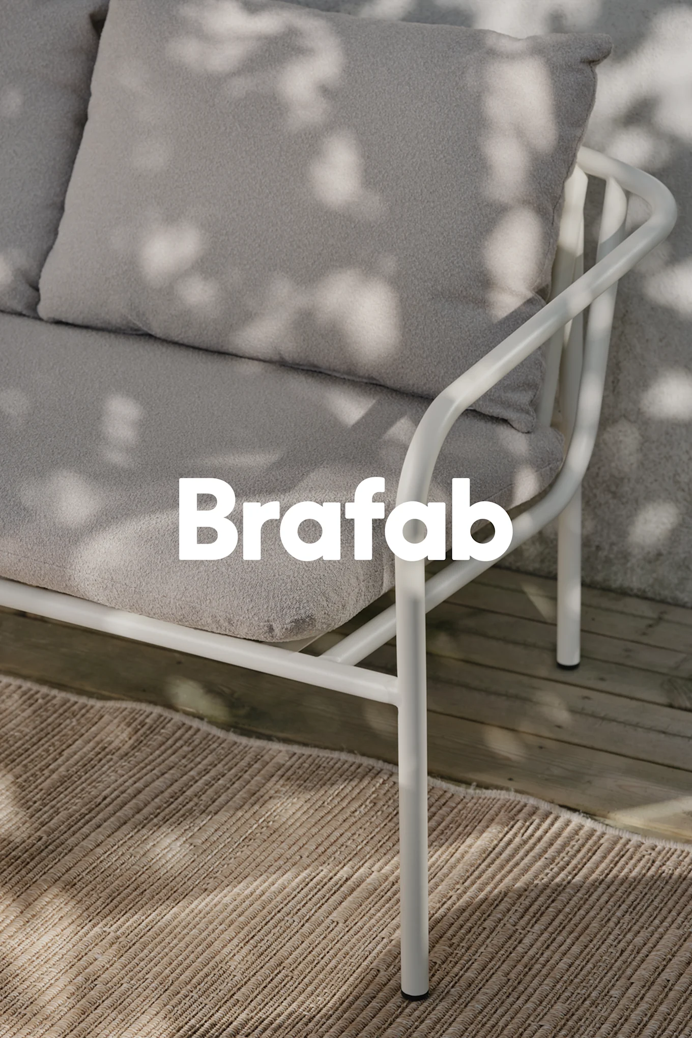 Brafab-logotyp över ljusgrå utomhussoffa, vit metallram, på beige matta på trädäck med fläckiga skuggor.