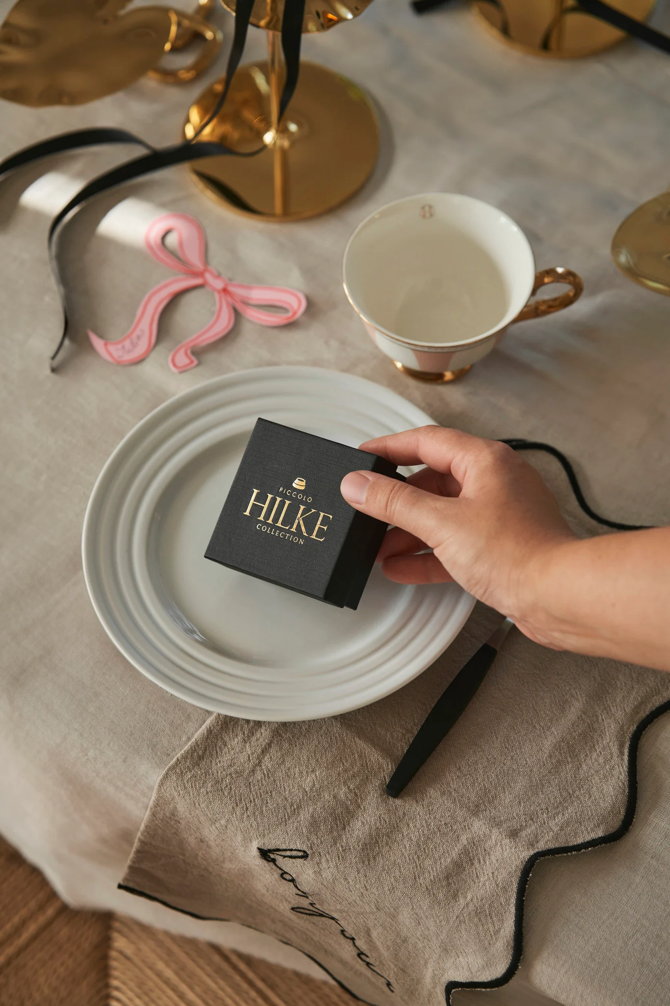 Fira Galentine's Day hemma med dina favoritpersoner. Här ser du en hand som placerar en ask från Hilke Collection på en bordsplacering som en liten present till dina gäster.