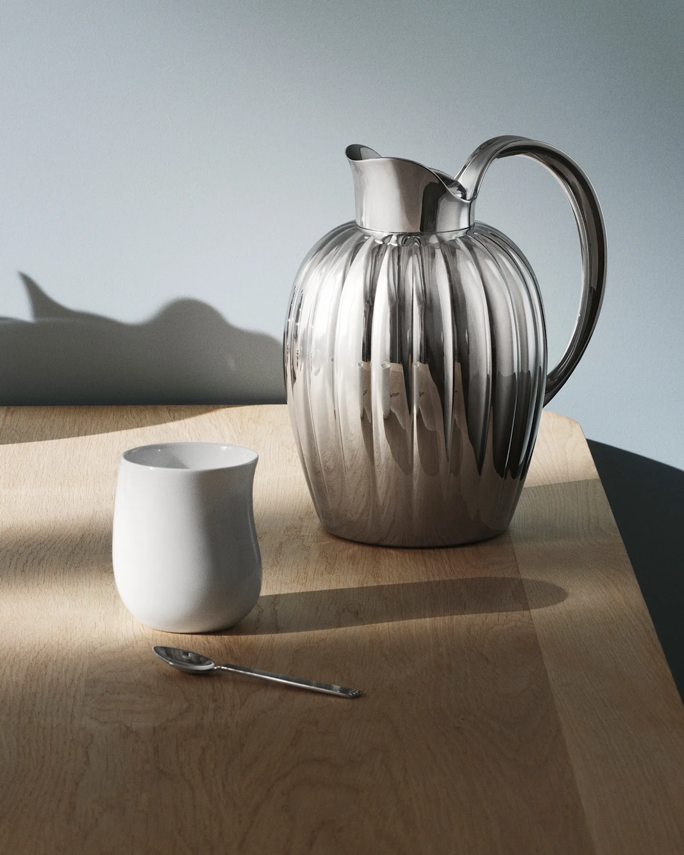 En glänsande, räfflad silverkanna med handtag står på ett mörkt, reflekterande bord, med ljusmönster på ytan.