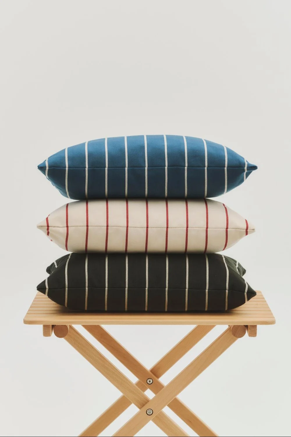 Staplade blå, creme och mörka randiga kuddar på ett fällbart träbord. Inspiration till din balkong 2026.