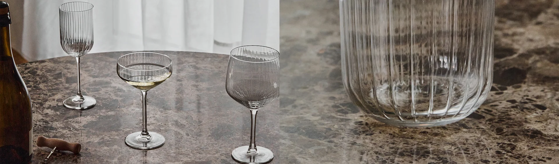 En flaska, korkskruv och tre olika räfflade glas på ett marmorbord, varav ett med vitt vin.