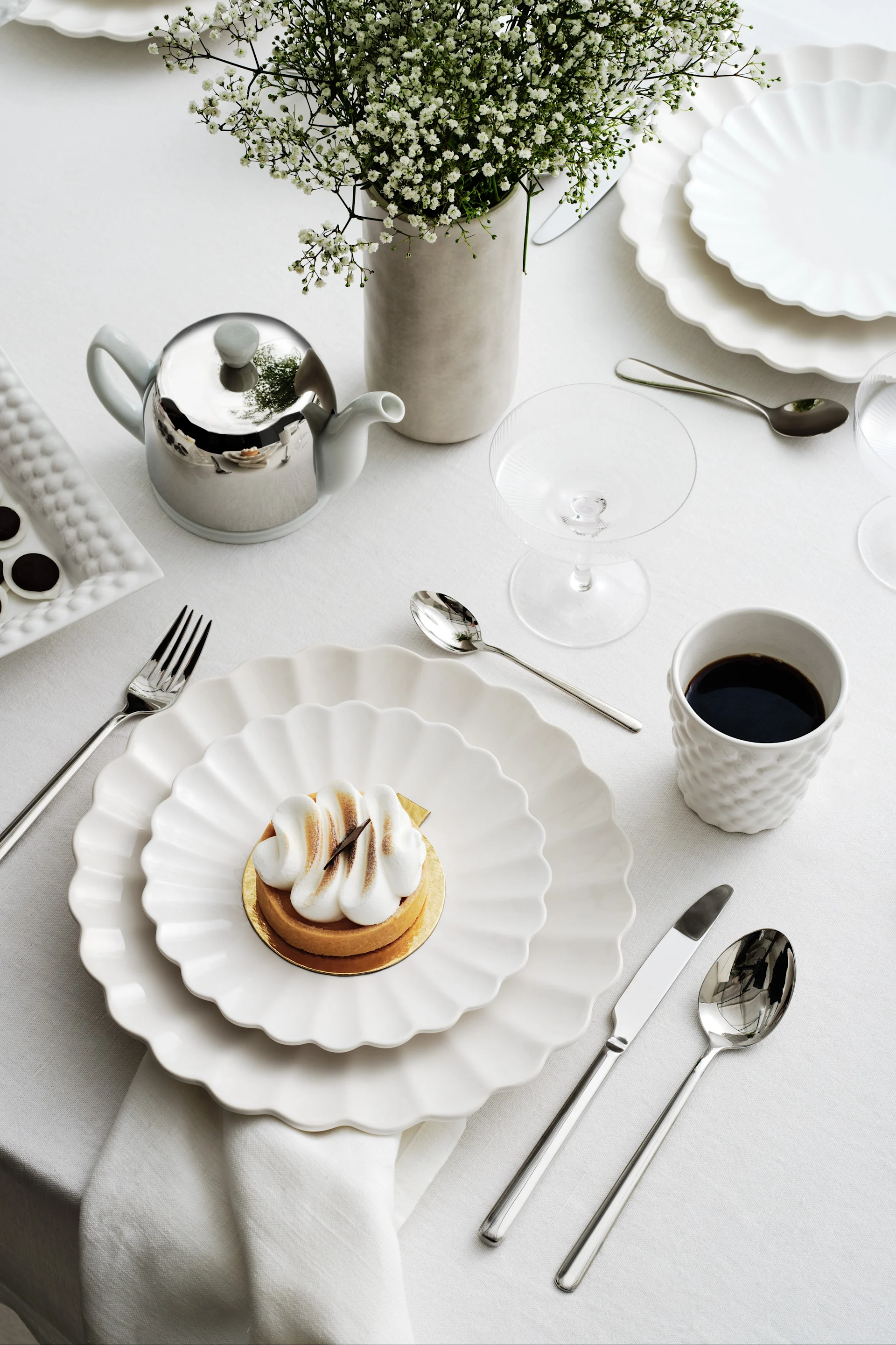 Elegant dukning med vita vågiga tallrikar, en marängtårta, kaffe, en silvertekanna och brudslöja.