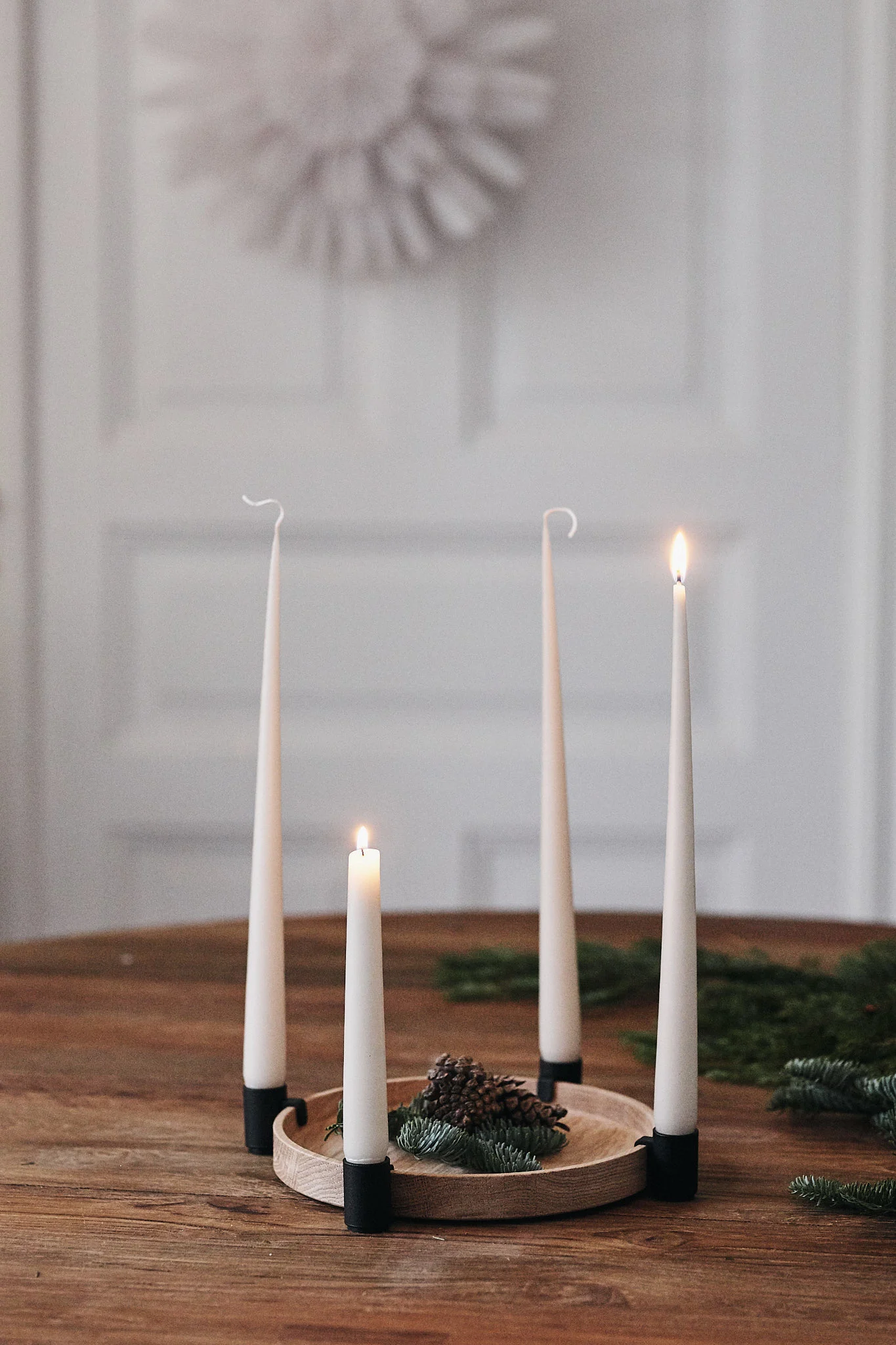 En rund adventsljusstake med fyra ljus står på ett bord och lyser med två av ljusen.