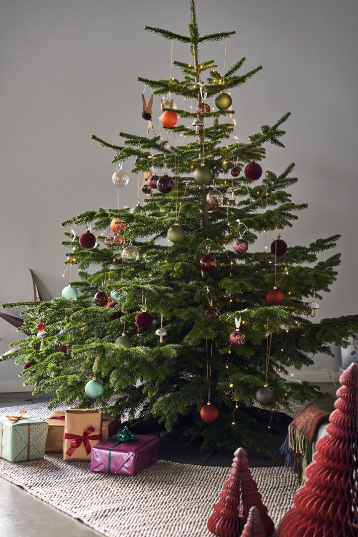 Dekorera julgranen med årets julgranspynt 2021 i 4 olika stilar enligt Nest Trends - Nurture, Share, Boost och Cultivate. Här ser du en pampig stor gran på Scandi Living Flock ullmatta i beige med ett tema av murriga färger och nyanser av rött, orange och grönt.