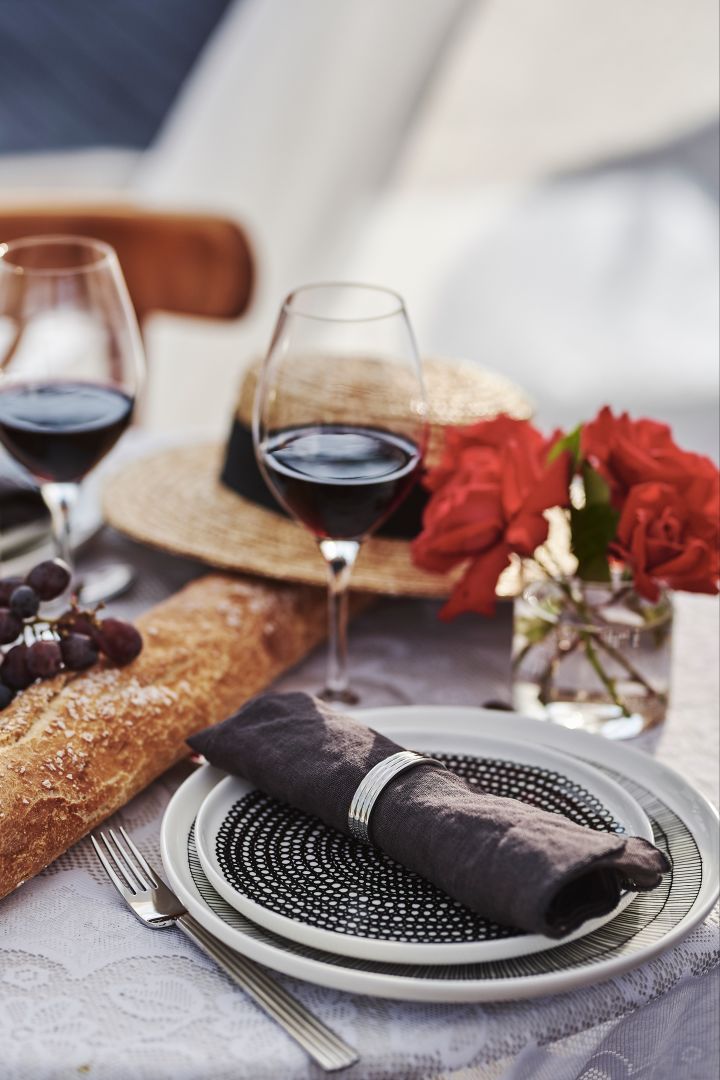 Dukning i fransk stil med svartvitt porslin, rödvinsglas och baguette på bordet. 