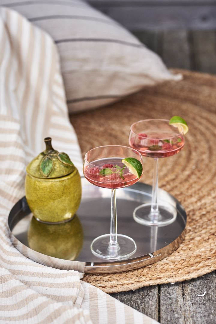Iittala Essence cocktailglas med god sommardrink i på silverbricka på jute matta vid havet.