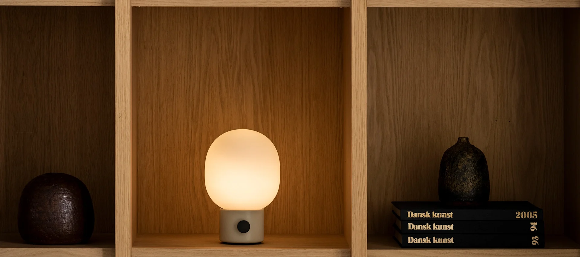 Vardagsrum hos Audo Copenhagen med JWDA bordslampa, svart hylla och vaser.