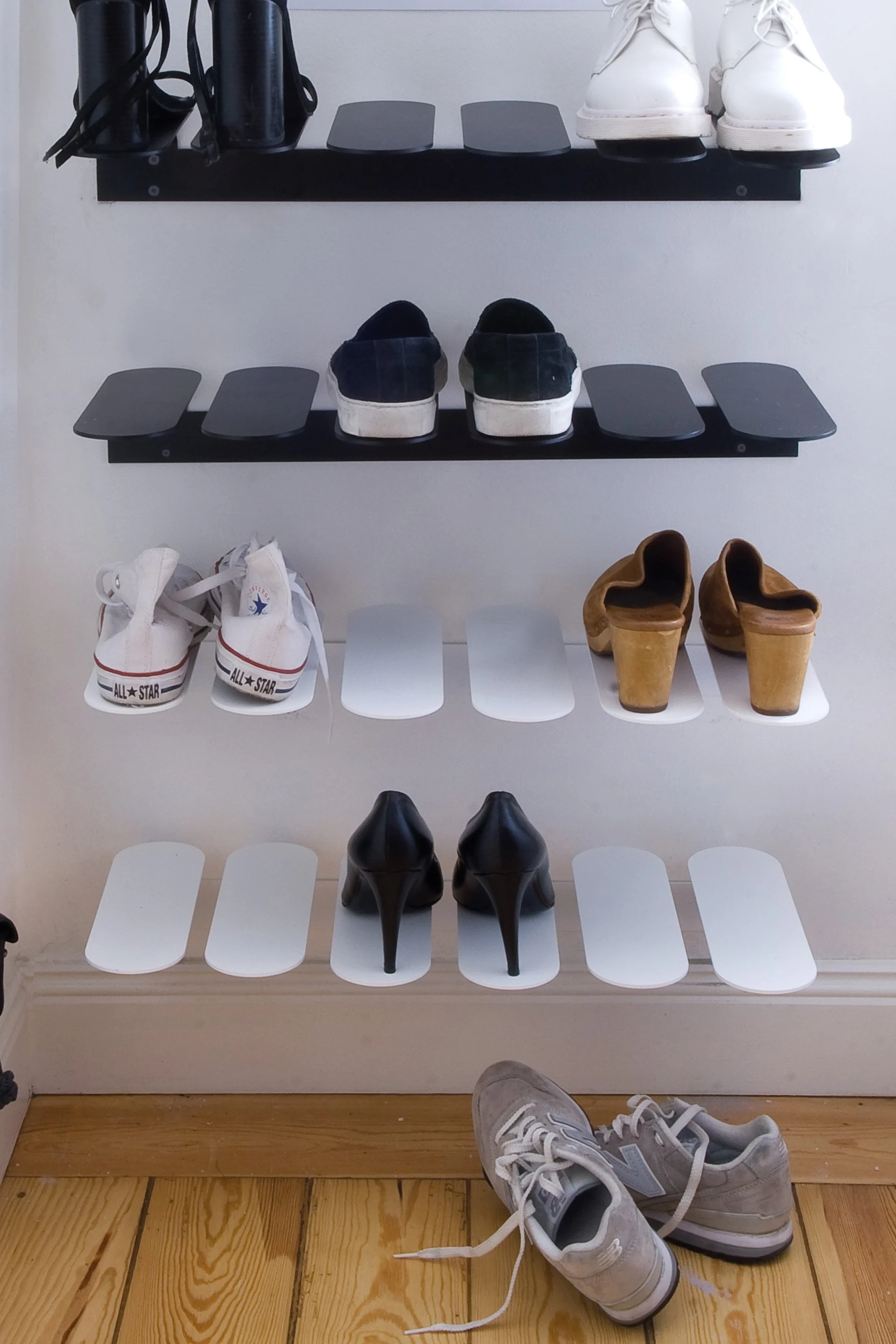 Diverse skor utställda på vägghyllor, inklusive svarta klackar, vita sneakers, mörka slip-ons, träskor och grå sneakers.