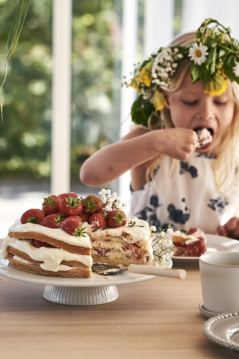 Duka avskalat till midsommar och servera jordgubbstårtan på ett vitt tårtfat - som här, där en flicka med blosmterkrona äter av tårtan.