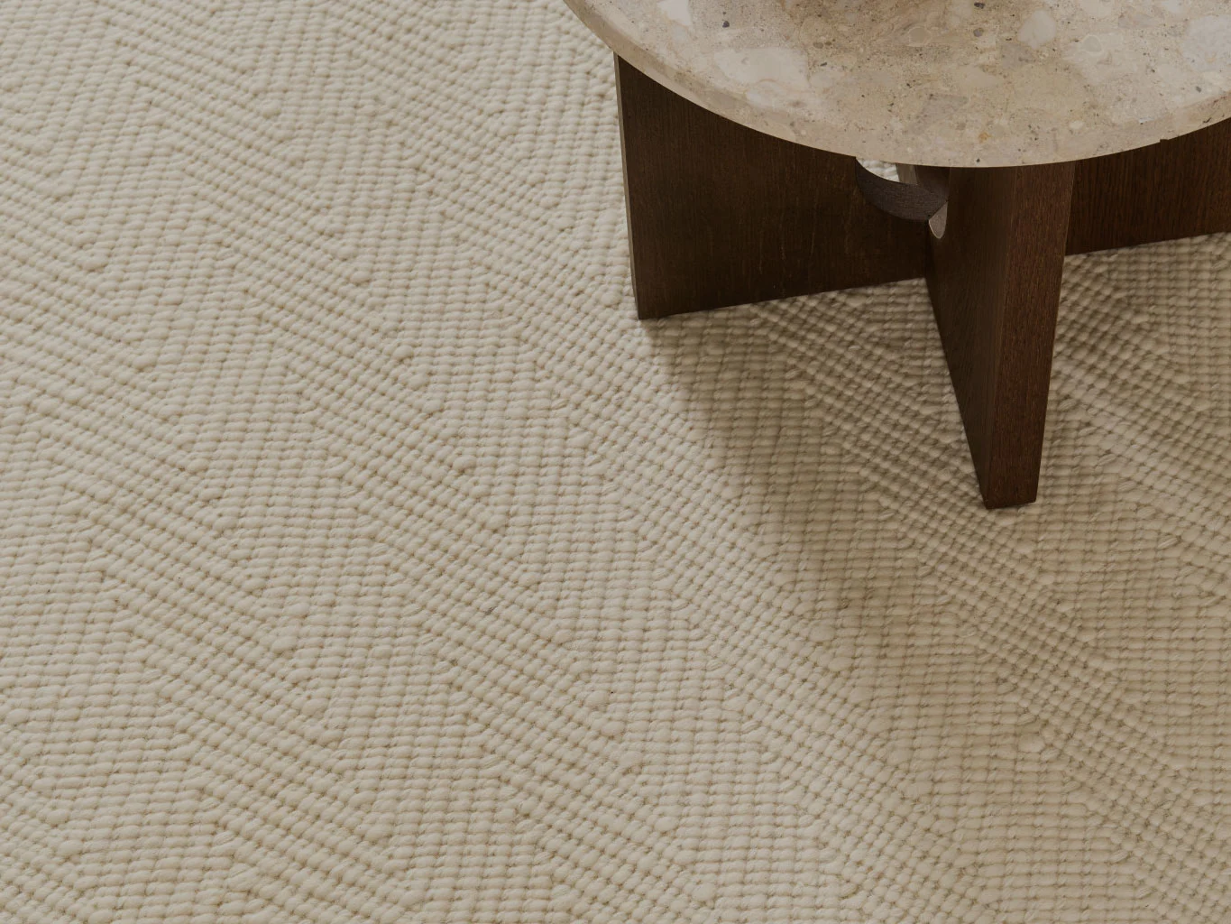 Närbild av en krämfärgad texturerad matta med sicksackmönster, bredvid ett bord med stenskiva.