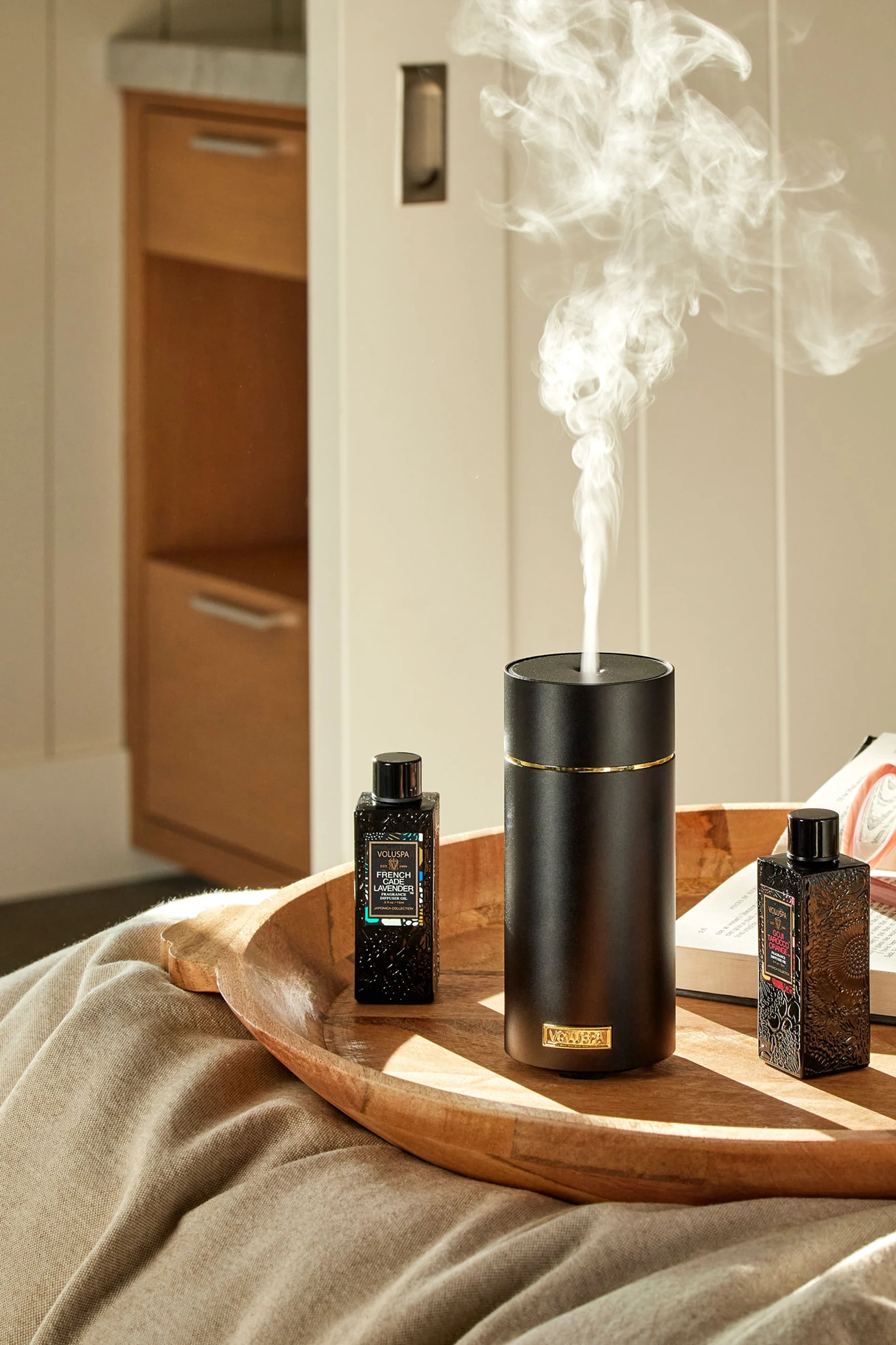 Den grå stendiffusorn från Volant står på en hög med böcker framför en spegel, med en växt bredvid. Ge bort den i present på mors dag för att skapa en spakänsla.