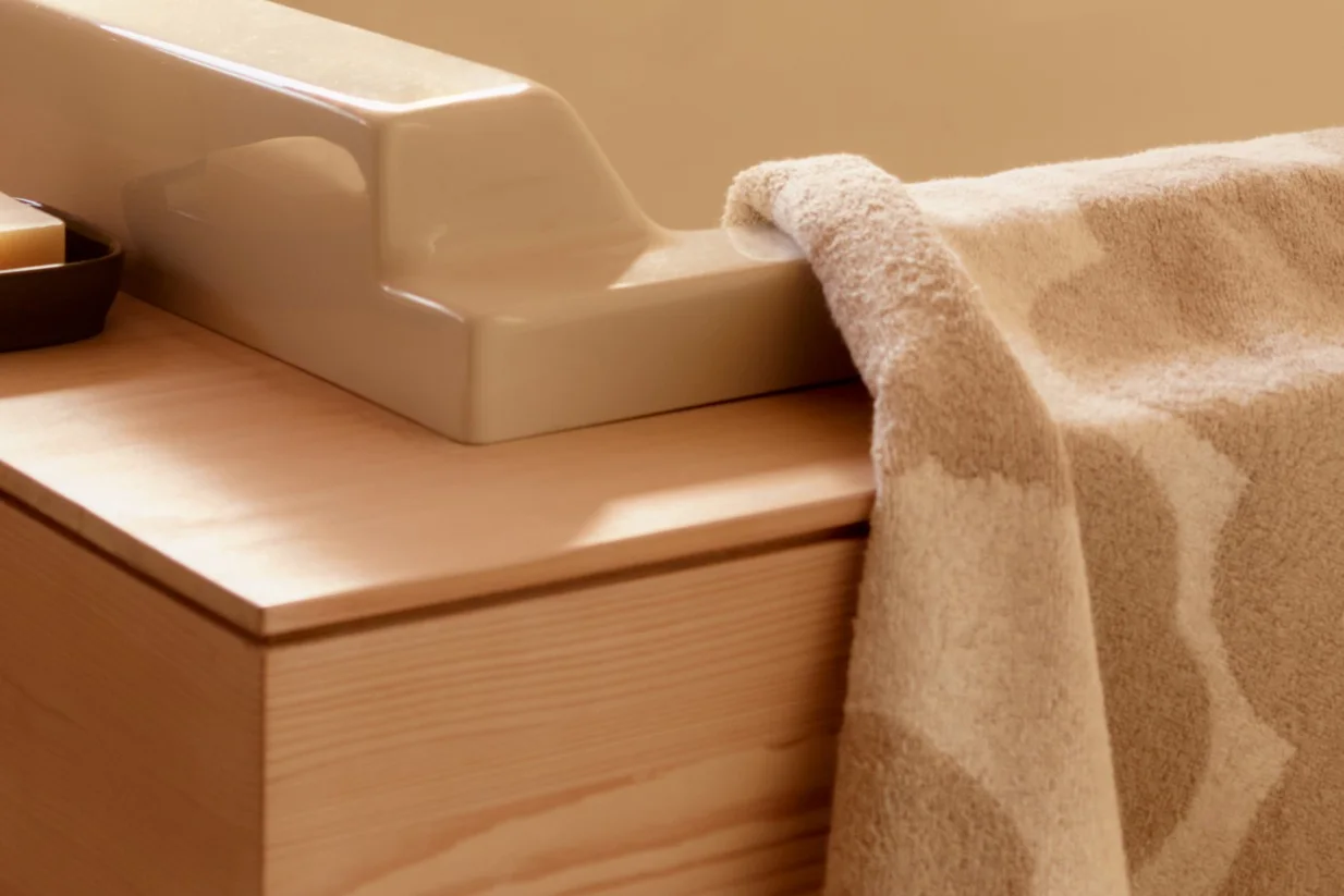 Närbild av en beige texturerad handduk draperad över en ljus keramisk armatur på en trätoalett med en tvål.