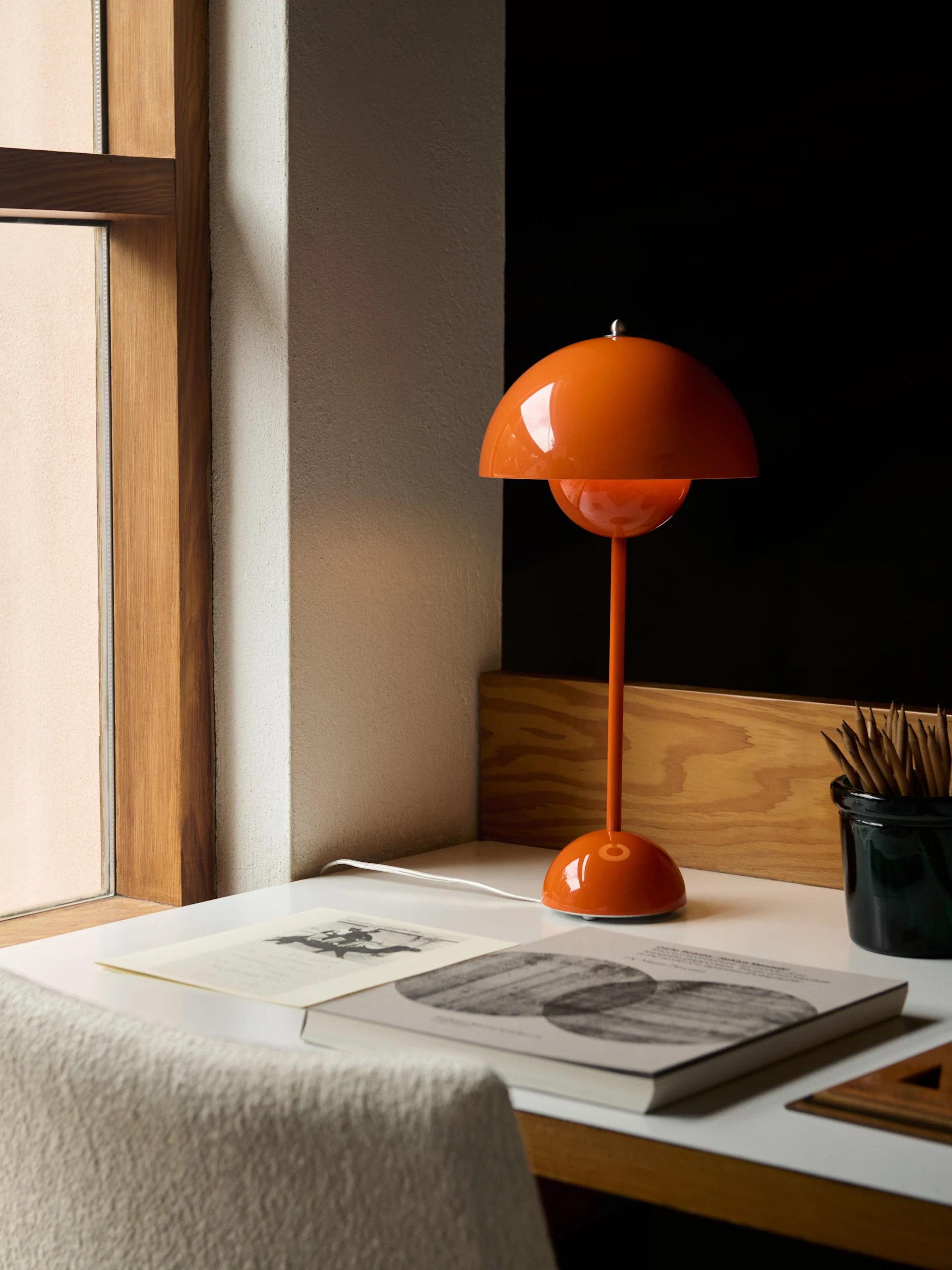 En orange kupolformad bordslampa står på ett vitt skrivbord bredvid böcker och en pennbehållare.