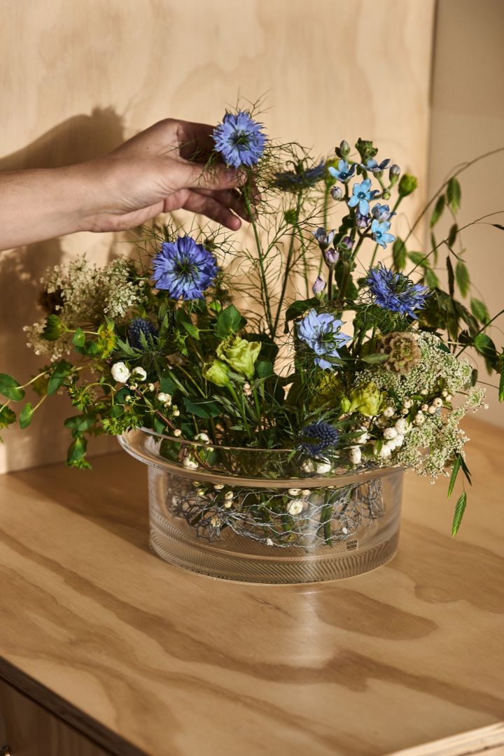 Limelight skål från Kosta Boda i klarglas med ett vackert blomsterarrangemang i av blå och gröna blommor. 