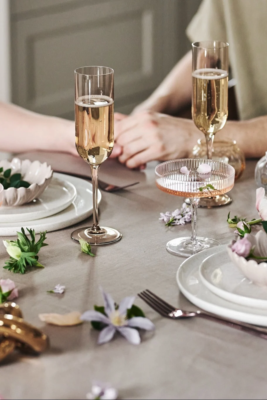 Du kan också dekorera bordet på ett lekfullt sätt för din romantiska måltid hemma. Här ser du vitt porslin, enkla glas och blommor på en beigefärgad duk.