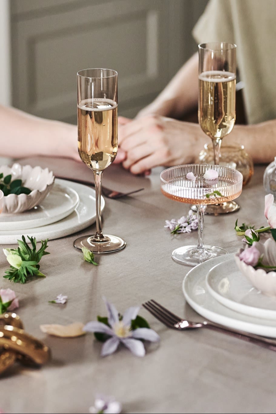 Du kan också dekorera bordet på ett lekfullt sätt för din romantiska måltid hemma. Här ser du vitt porslin, enkla glas och blommor på en beigefärgad duk.