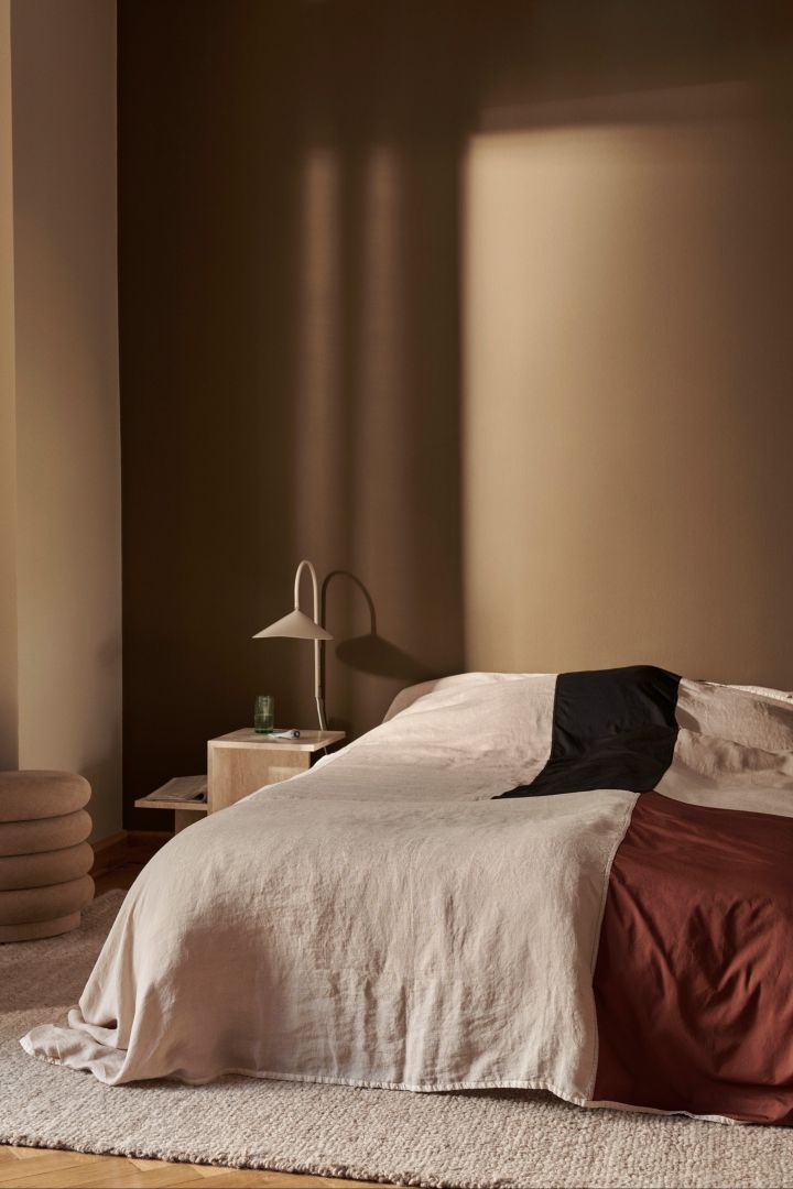 Arum vägglampa från Ferm Living, här i sovrum med bruna väggar och ljus matta, en vägglampa som är perfekt som sovrumslampa.