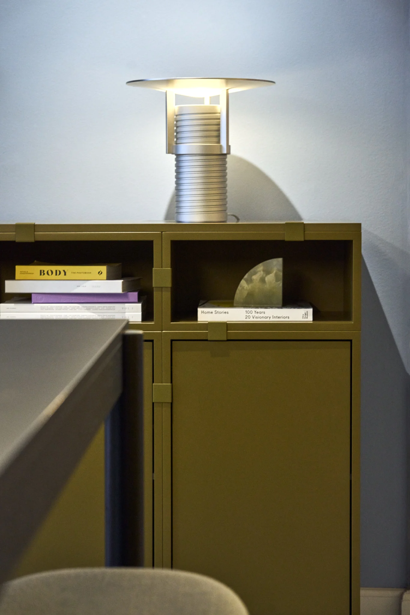 En grön hylla, byggd från Stacked-kollektionen, med den silverfärgade Set-bordslampan ovanpå, allt från Muuto.