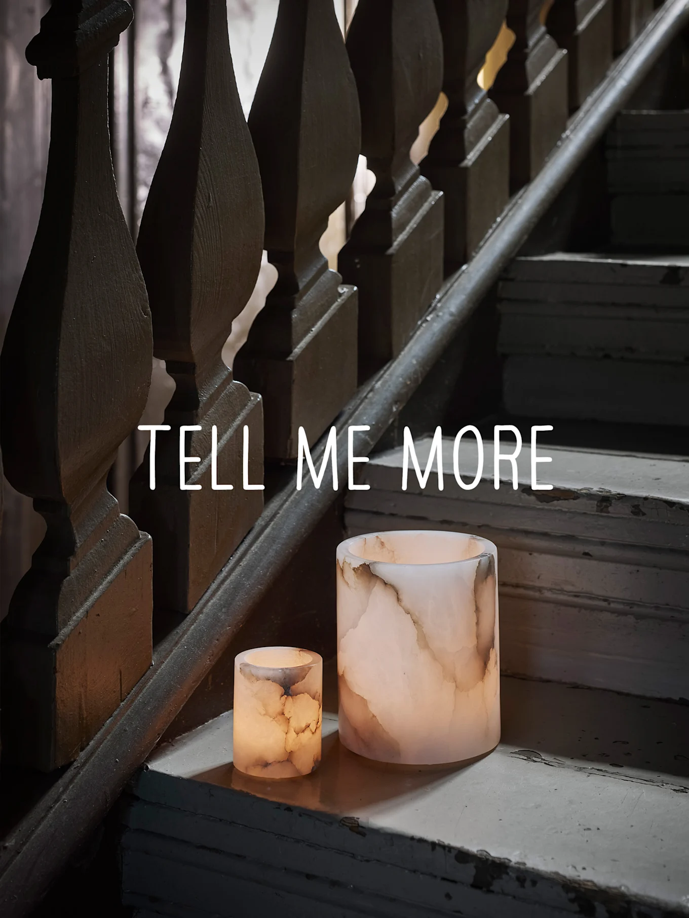 Två glödande onyxliknande ljushållare på en sliten trätrappa, med texten "TELL ME MORE".