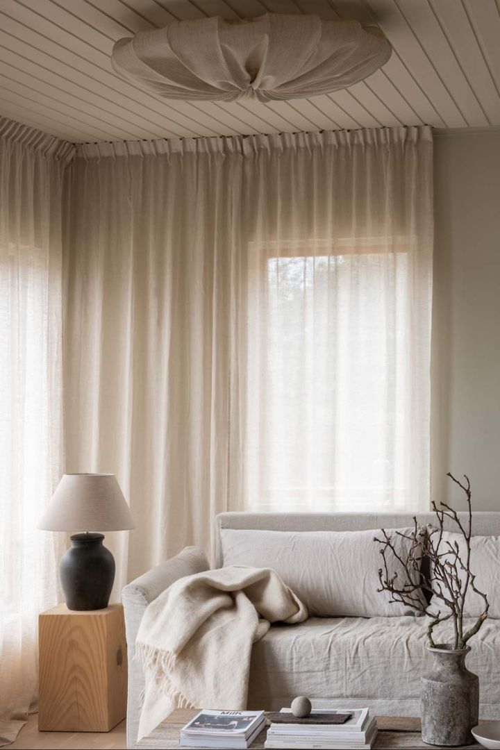 Ljust vardagsrum med beige soffa och ljusa gardiner, i taket hänger Anna plafond i linnetyg från Watt & Veke.