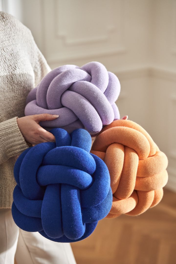 Knot-kuddar från Design House Stockholm i blå, lila och aprikosfärg i famnen på en kvinna. 