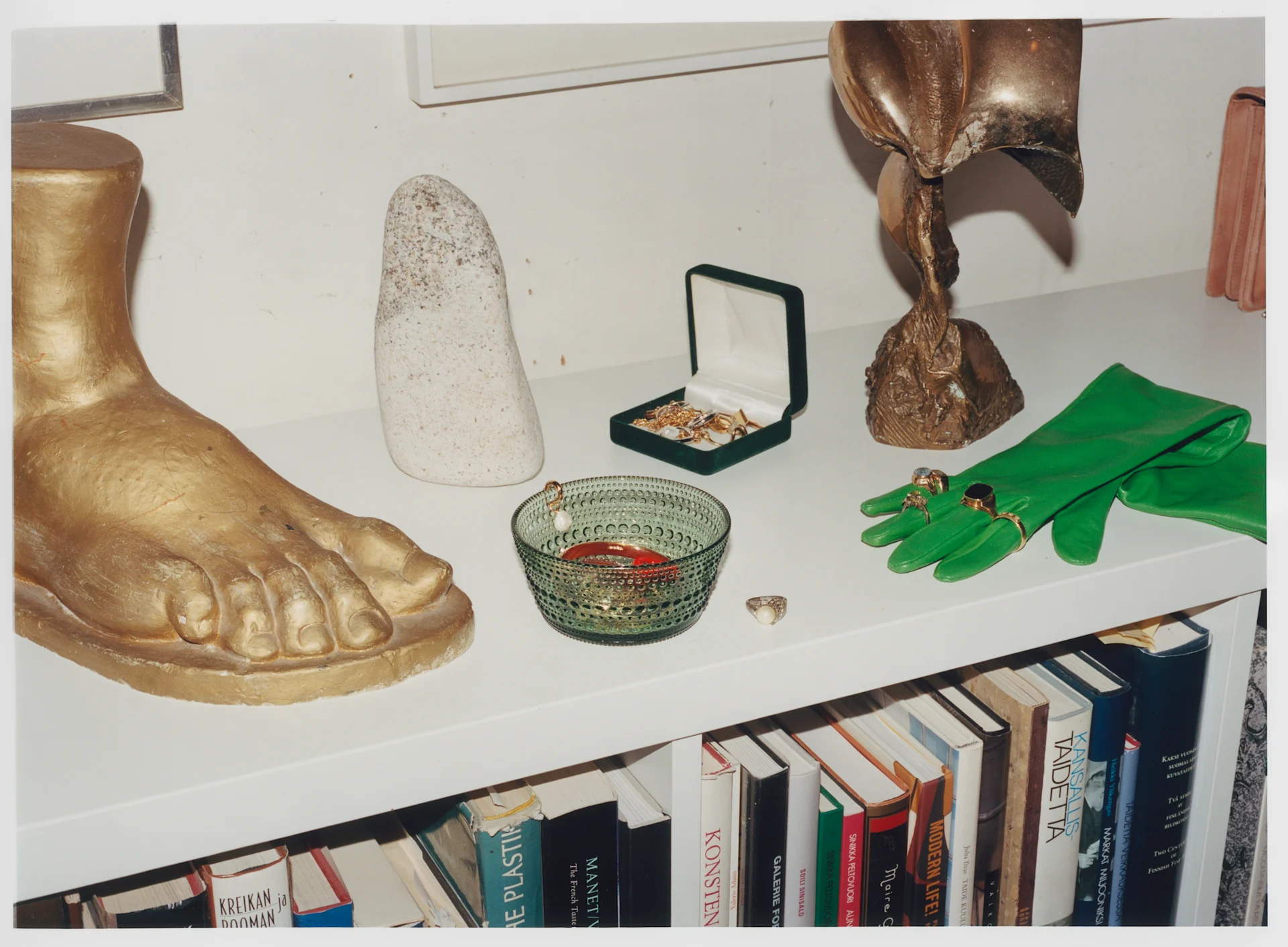 Iittala kliver in i ny era men produkterna är desamma, här Kastehelmi-skål i grönt på en skänk med statyer och handskar.