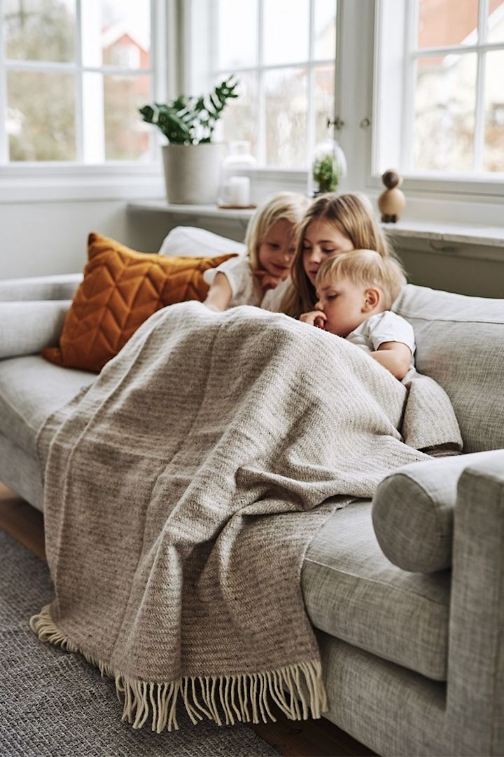 Barnen myser i soffan under en värmande ullpläd från Klippan Yllefabrik. 