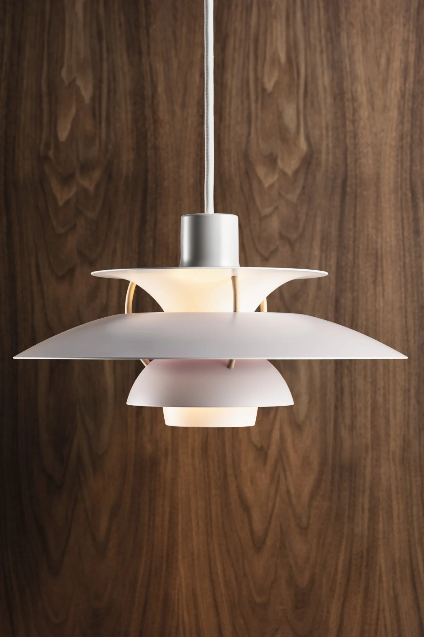 En vit flerskiktad taklampa med ett varmt sken, hängande mot en vägg av mörka träpaneler.