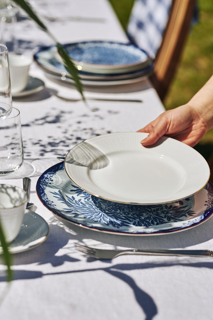 En klassisk midsommardukning med blåvitt porslin. Här Ostindia Floris mattallrik i kombination med assietten Swedish Grace Gala - vit tallrik med guldkant.