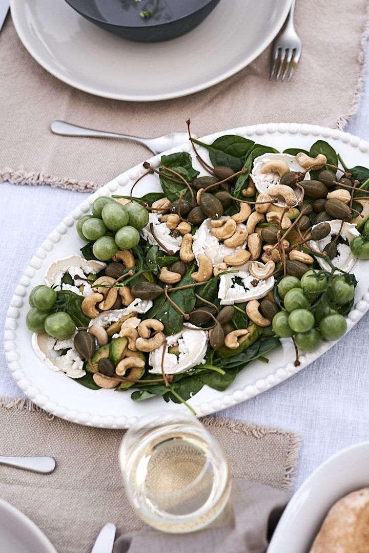 En vegetarisk sommarsallad gjord på getost, babyspenat, tomat och cashewnötter serverad på ovalt serveringsfat från PotteryJo. 
