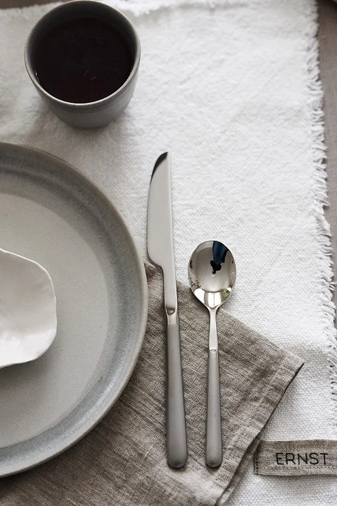 Gense Ehra bestick förskönar en rofylld frukostdukning på en beige linneservett ihop med rustika tallrikar från Paradisverkstan.