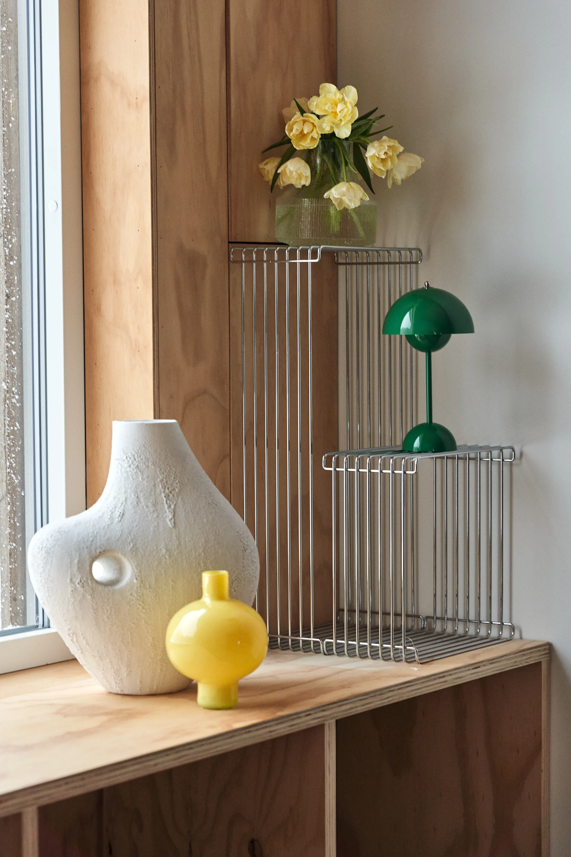 Stilleben - inredning som får hemmet att poppa. Här ett hörn i vardagsrummet som livats upp med grön VP9:a lampa, Panton Wire-hyllor och gul vas.