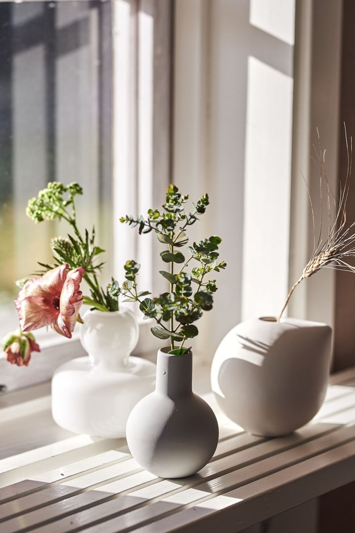 Flera små vaser för snittblommor står på en fönsterbräda. 