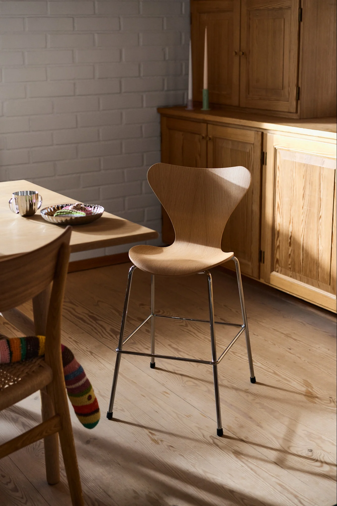 Den danska designklassikern Sjuan stolen från Fritz Hansen står i ett rum där det ljusa träslaget harmonierar med rummets övriga inredning från trägolvet till bokhyllan i bakgrunden.