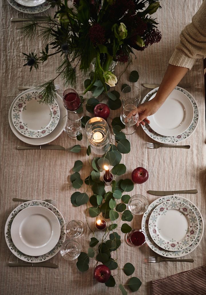 En enkel och elegant julbordsdukning fotograferad uppifrån med gröna blad och röda äpplen som dekoration.