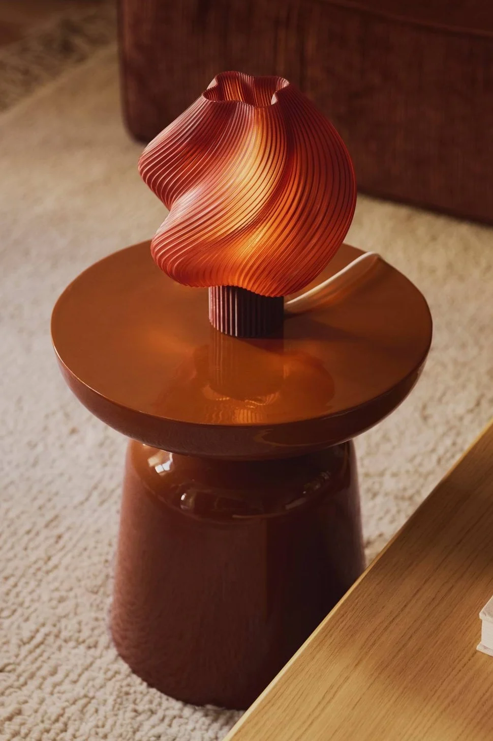 En varmt upplyst, vågig orange veckad lampa står på ett glansigt brunt sidobord.