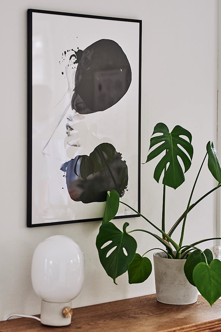 Monokrom poster, en kruka i betong och JDWA bordslampa från Menu utgör ett stilleben i matplatsen vars inredning går i skandinavisk stil. 