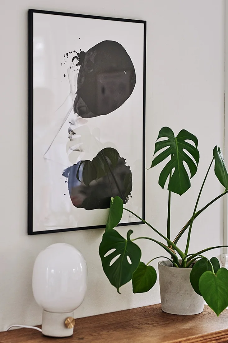 Monokrom poster, en kruka i betong och JDWA bordslampa från Menu utgör ett stilleben i matplatsen vars inredning går i skandinavisk stil.