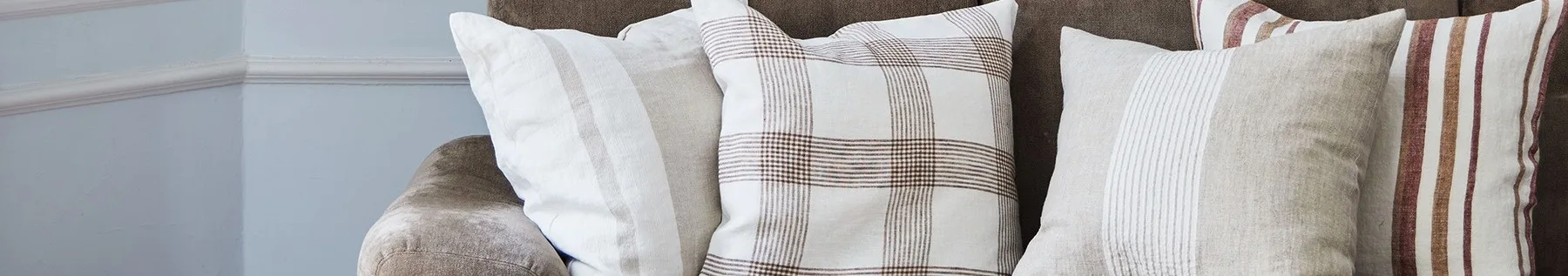 Närbild av tre kuddar på en brun soffa, med vita, beiga och rutiga mönster med bruna och röda ränder.