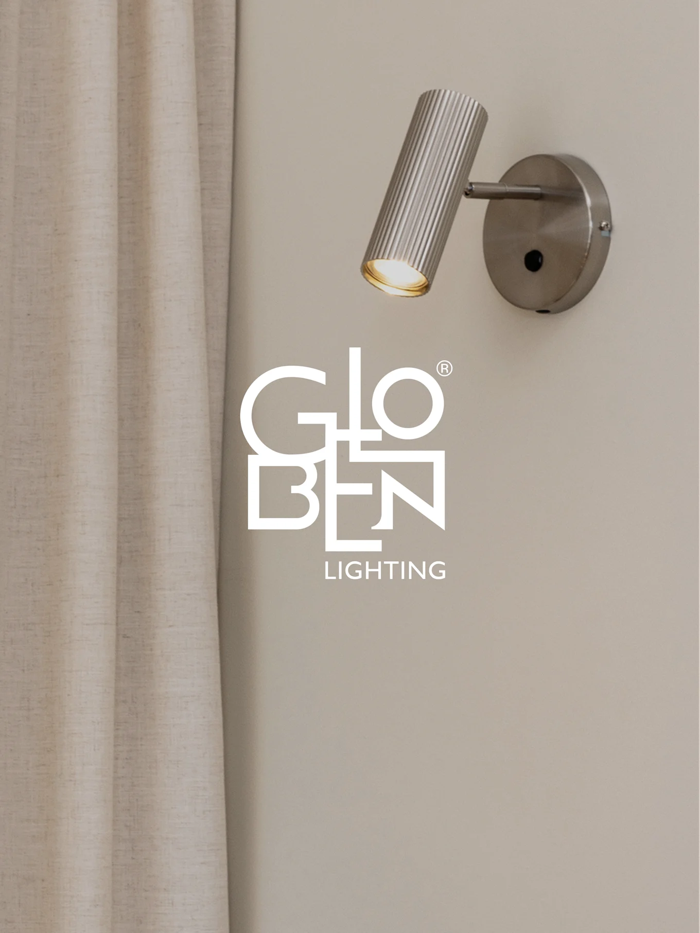 En borstad, räfflad väggspotlight i metall med ett varmt sken, bredvid en ljus gardin, med Globen Lighting-logotypen.