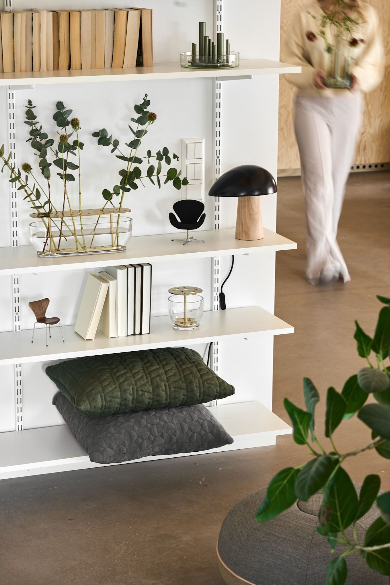 En vit bokhylla fylld med design från Fritz Hansen i form av Ikebana-vaser, Night Owl-bordslampa och kuddar i stilrent hem. 