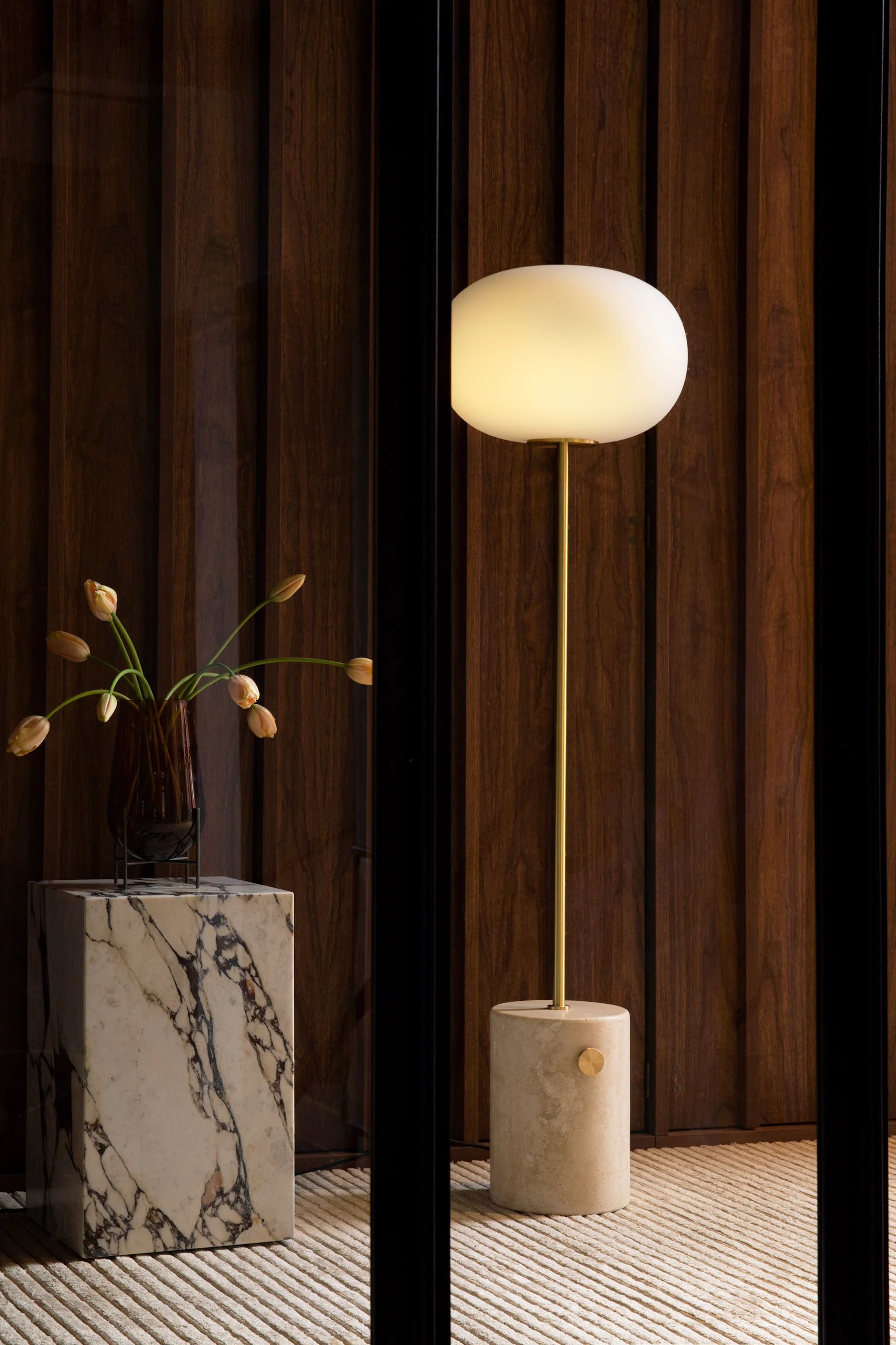 JWDA golvlampa i travertin från Audo Copenhagen, tidigare kända som MENU i stirent vardagsrum med travertin sidobord och vas på bordet. 
