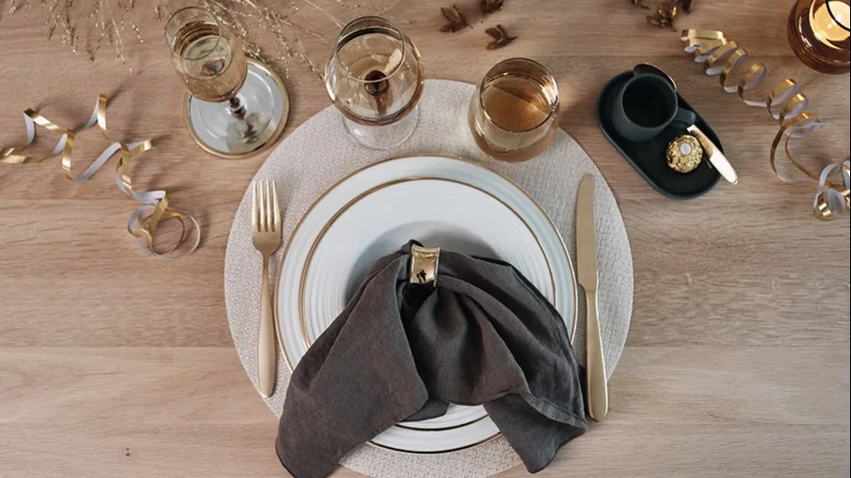 Nyårsdukning i guld med vita tallrikar med guldkant från Aida, guldbestick och bärnstensfärgade glas.