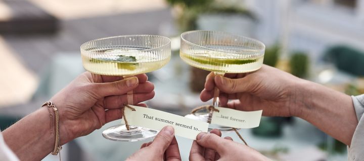 Placeringskort med sommarlåtar knutna runt foten av champagneglaset Ripple från Ferm Living är ett smart tips till trädgårdsfesten.