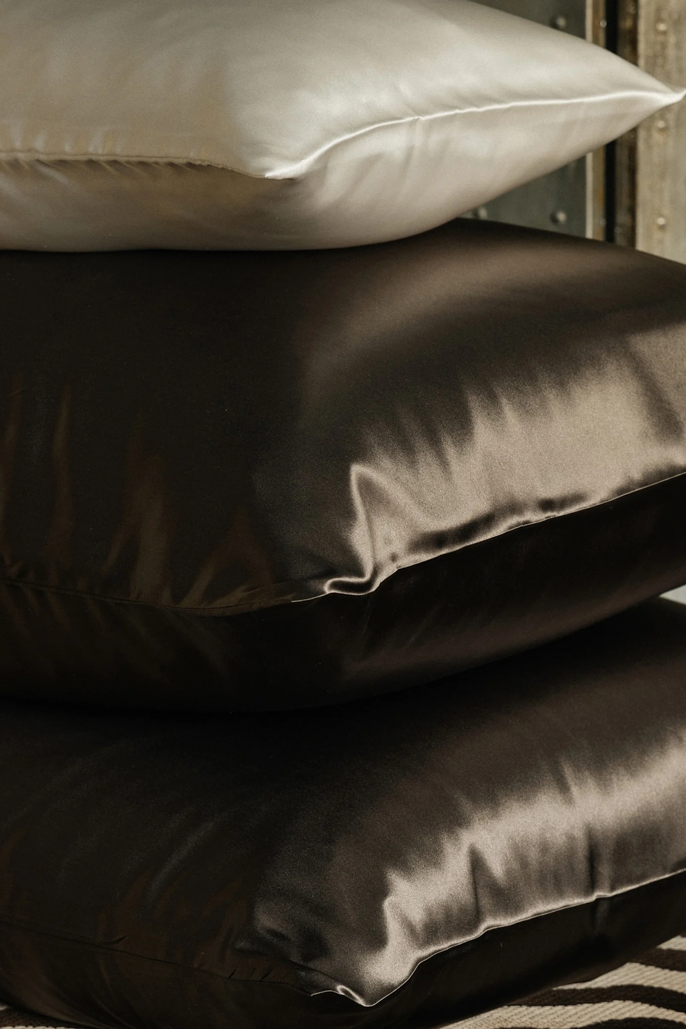 Stapel med tre sidenkuddar, en ljus och två mörkbruna.