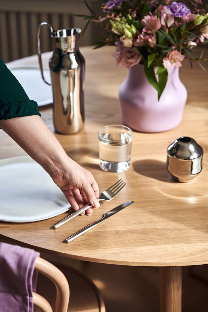 Enkel dukning med Dorotea-bestick från Gense samt vattenkaraff och vaser ur samma serie. Här ser du en hand som lägger ner Dorotea-bestick.