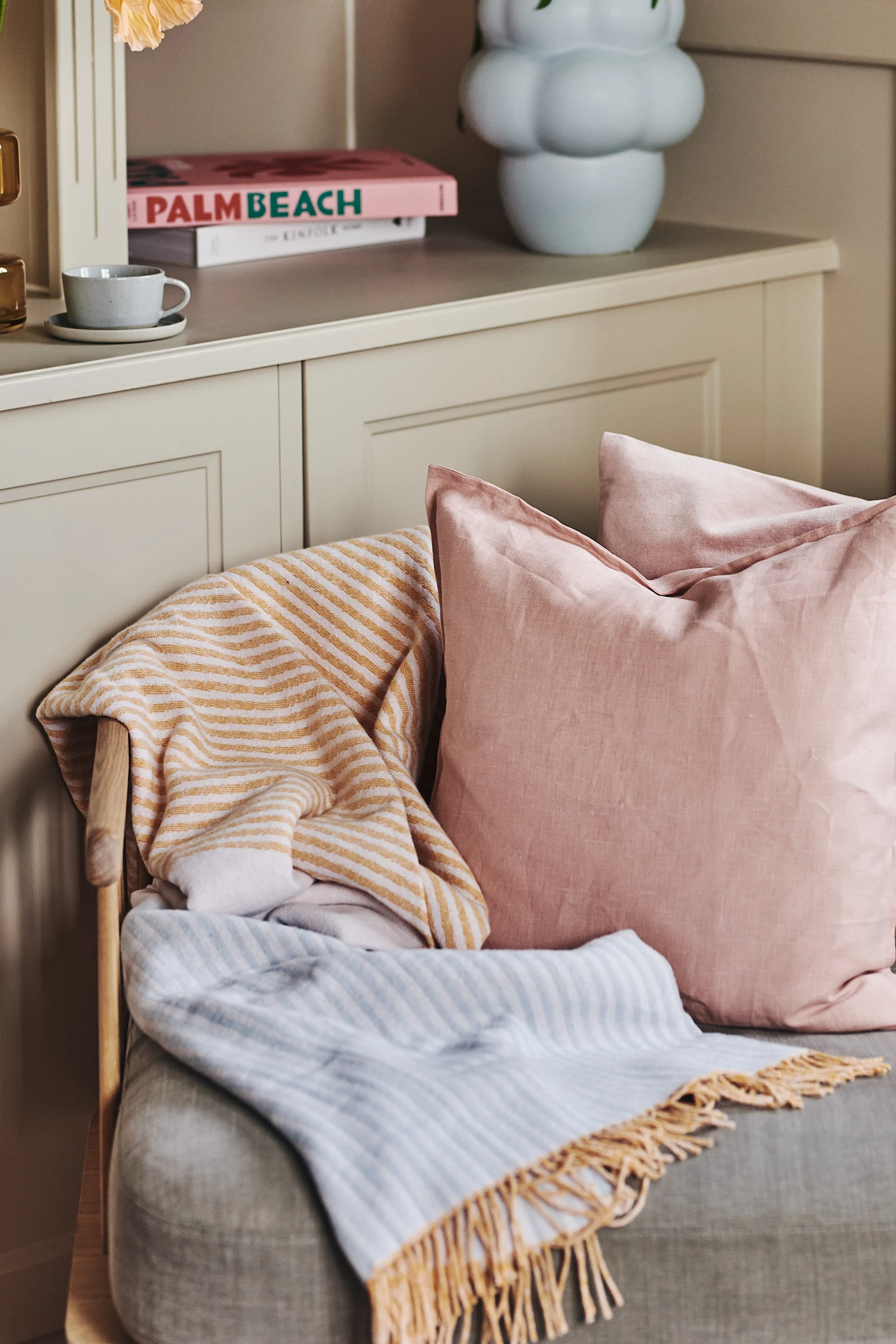 För in pastell i din inredning genom att inreda med Stripes bomullspläd från NJRD i gula, orangea och blå toner tillsammans med Calm kudde i Dusty rose från Scandi Living.